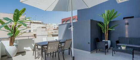 A rooftop terrace with a table and chairs, a large umbrella, and potted plants.