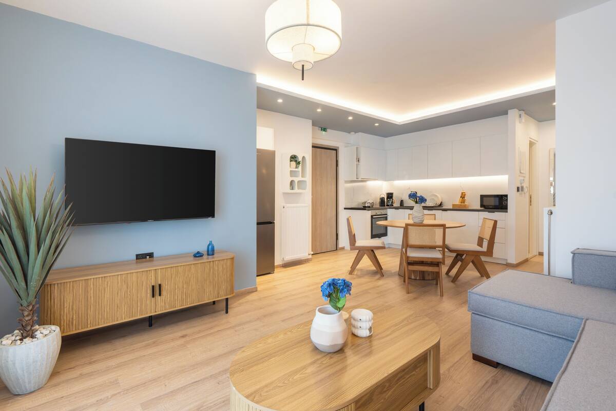 A modern living room with a flat-screen TV, wooden furniture, a dining area, and a kitchen.