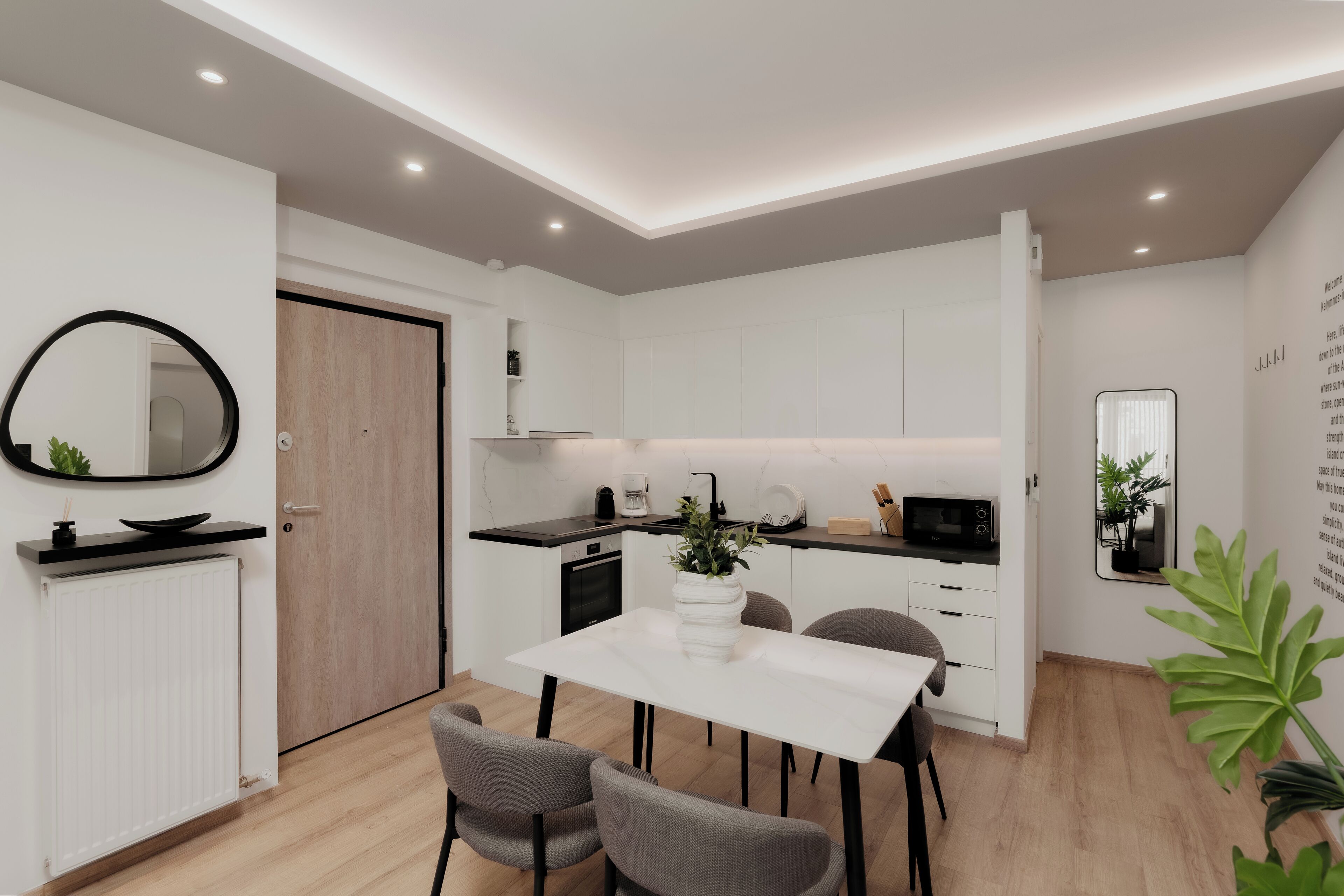 Una cocina moderna con armarios blancos, una mesa de comedor con sillas y un espejo grande en la pared.
