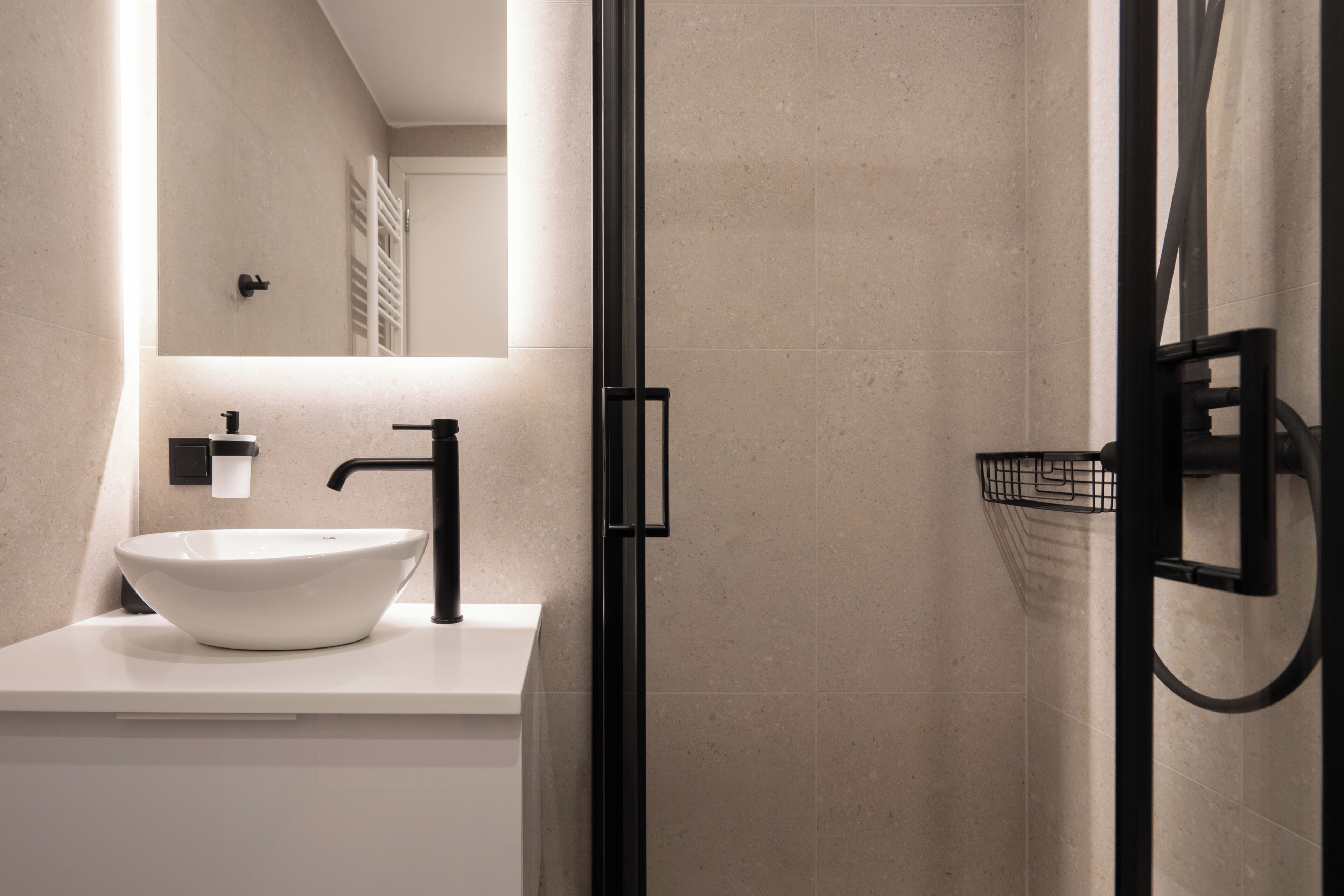 Ein modernes Badezimmer mit einem weißen Waschbecken, einem schwarzen Wasserhahn und einer Duschkabine aus Glas.