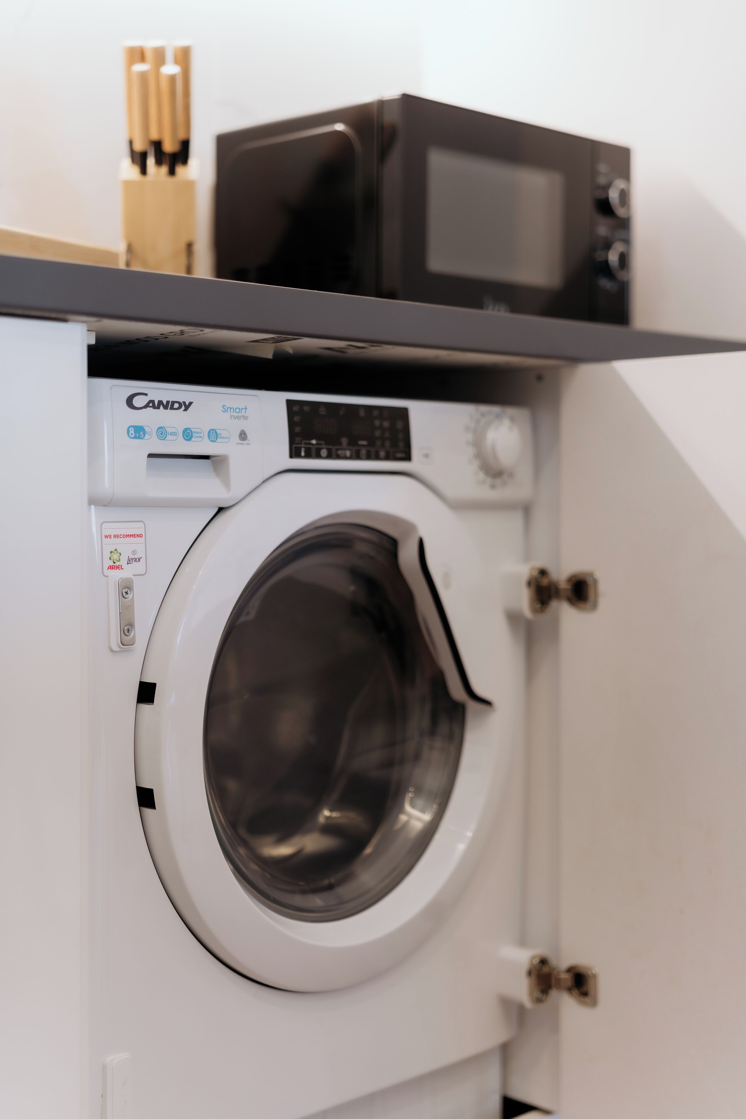 A front-loading washing machine with a control panel, a microwave above it, and a wooden utensil holder.