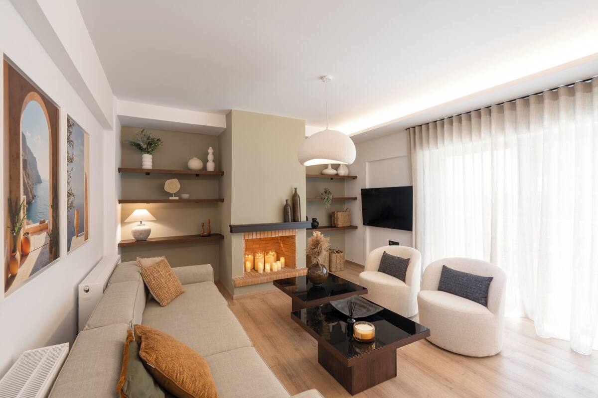 A modern living room with a sofa, armchairs, a coffee table, a fireplace, and a television.