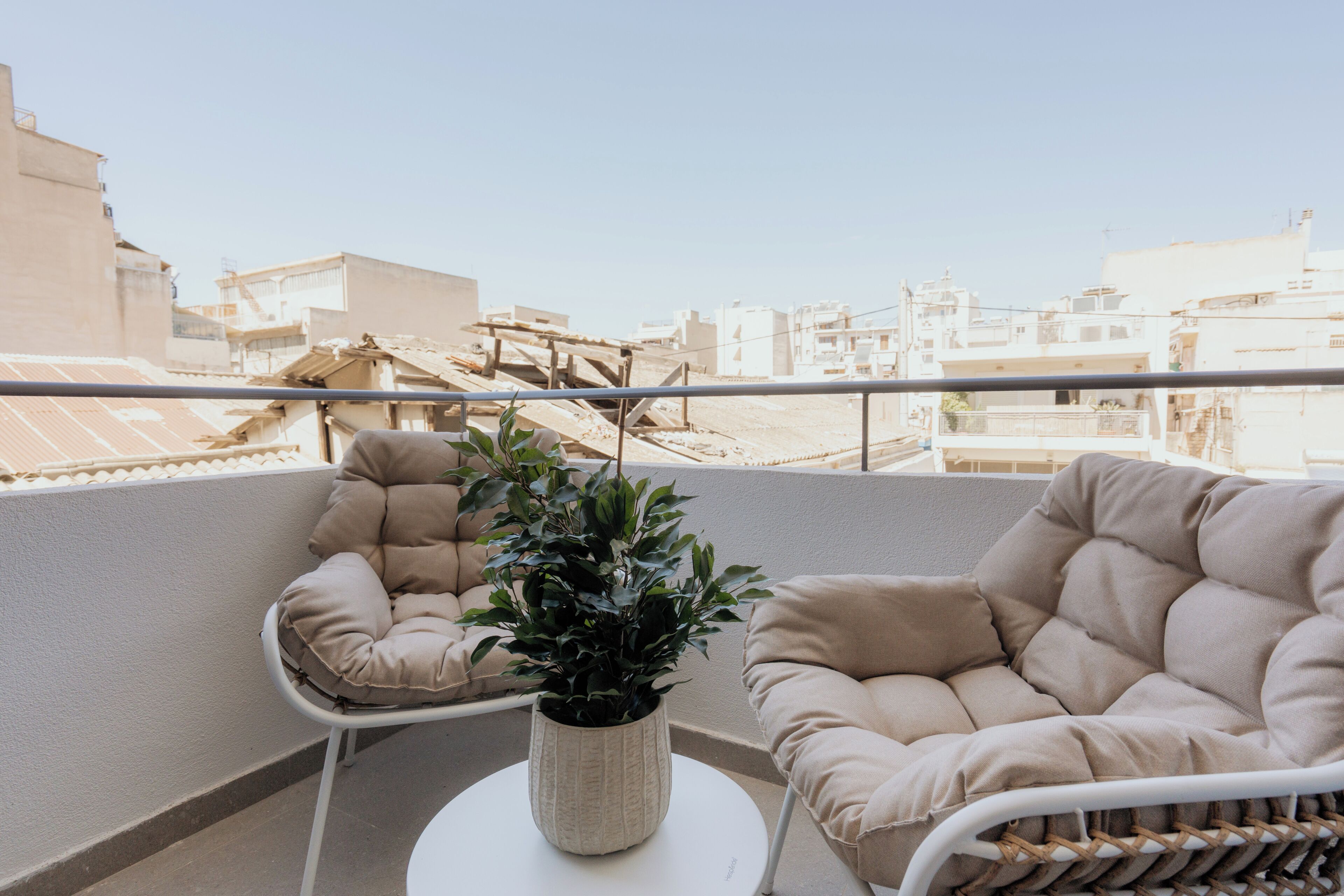 A balcony with two beige cushioned chairs, a white table, and a potted plant.