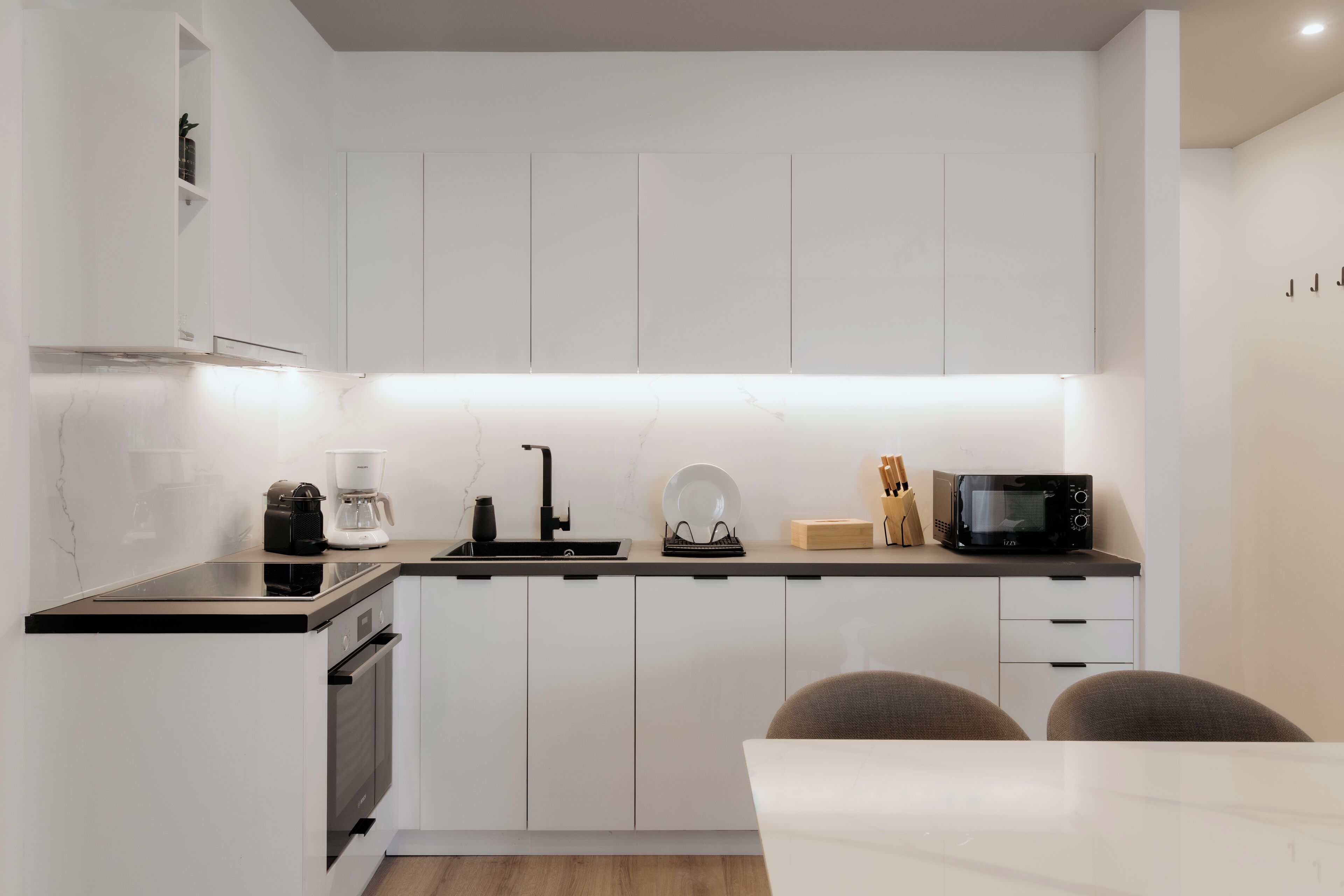A modern kitchen with white cabinets, a black countertop, a coffee maker, a microwave, and a sink.