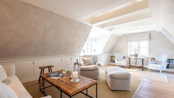 Un dormitorio estilo loft con techo alto, vigas a la vista, una mesa de centro de madera, un sofá, un reposapiés y una ventana con vistas.