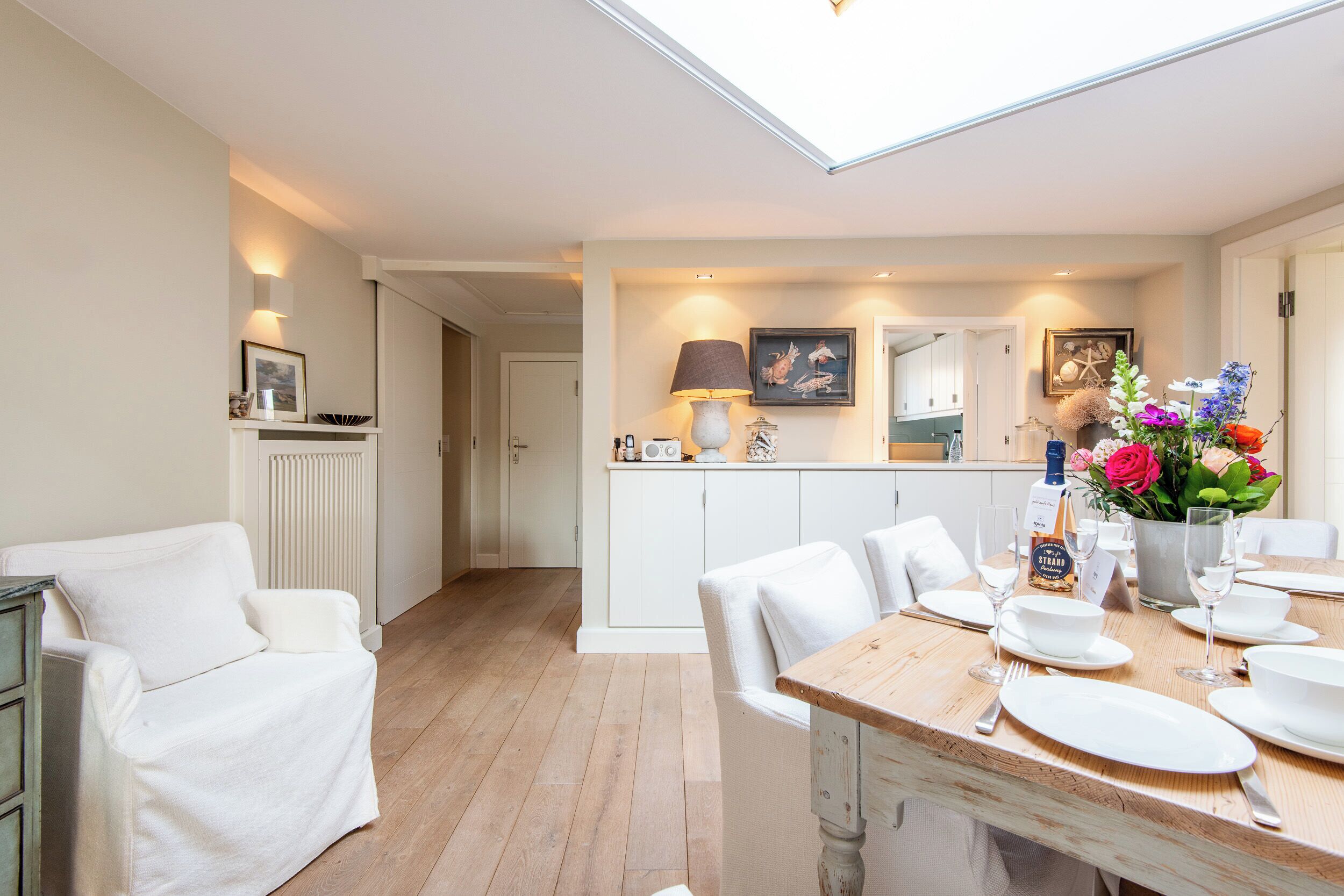 Una cocina moderna con armarios blancos, un comedor con mesa de madera para cuatro personas y un espacio de sala de estar acogedor con un sofá blanco.