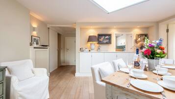 Una cocina moderna con armarios blancos, un comedor con mesa de madera para cuatro personas y un espacio de sala de estar acogedor con un sofá blanco.