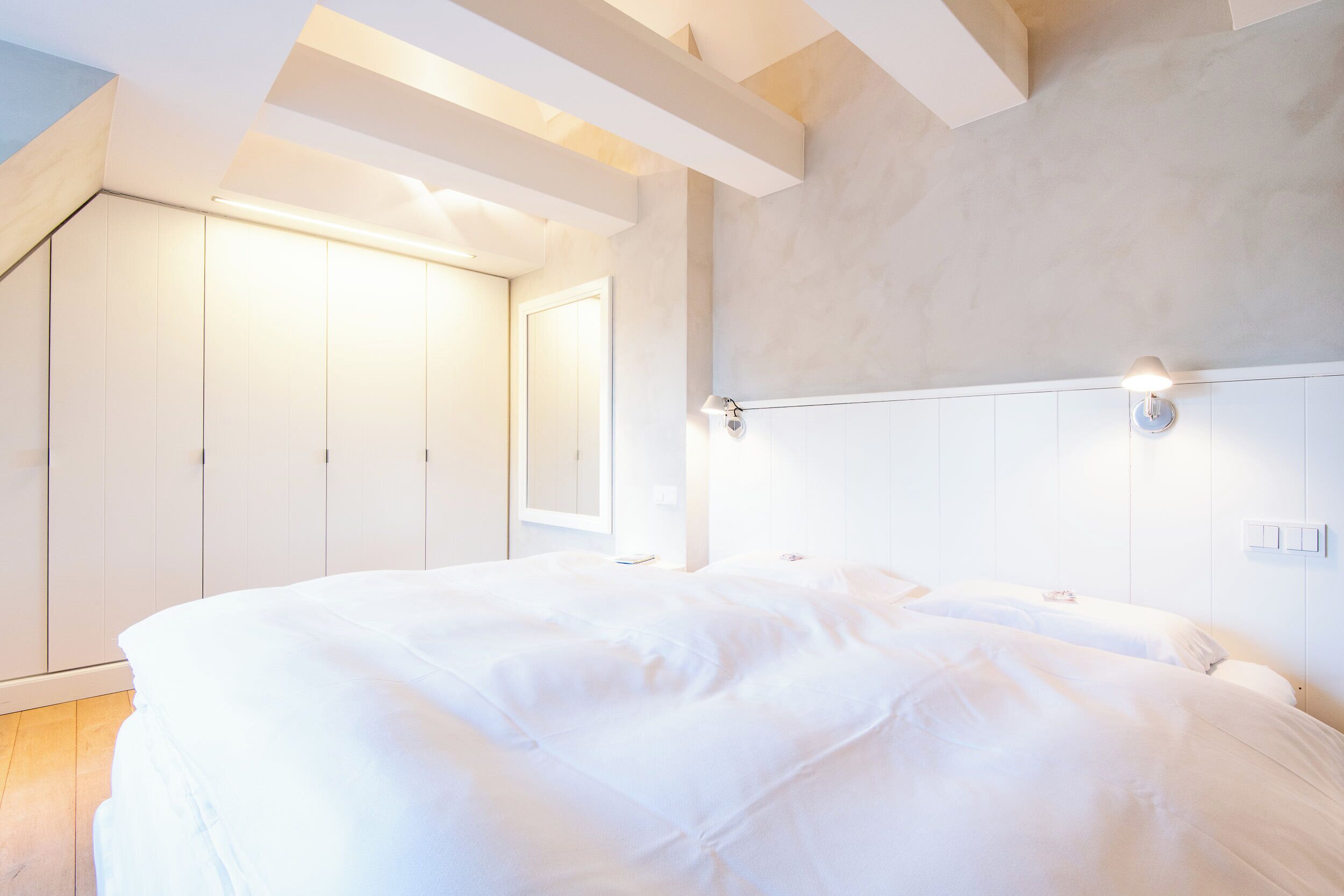 A bedroom with a large bed, a wardrobe, and a wall-mounted light fixture.