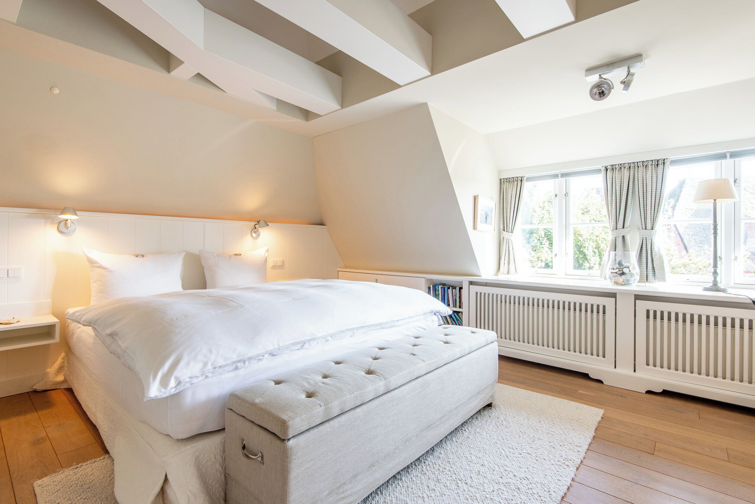 A bedroom with a large bed, bedside lamps, a radiator, and a window with curtains.