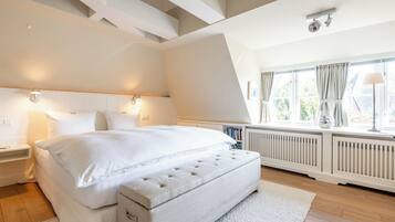 Ein Schlafzimmer mit einem großen Bett, Nachttischlampen, einem Heizkörper und einem Fenster mit Vorhängen.