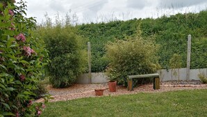 Un jardín con un banco, plantas en macetas y un césped.