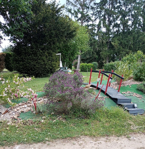 A garden with a wooden bridge, a small hill, and various plants.