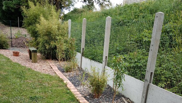 Un jardín con un sendero de grava, un seto bajo y un muro de contención de hormigón.