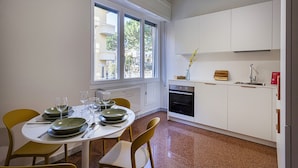 Cocina compacta con armarios blancos, horno empotrado y ventana que proporciona luz natural.
