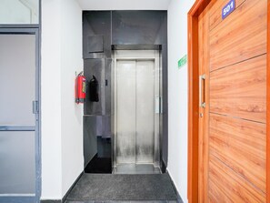 A hallway with a fire extinguisher, a door with a number sign, and a wooden door.