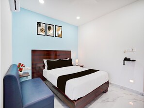 A hotel room with a bed, a nightstand, a lamp, a blue chair, and artwork on the wall.