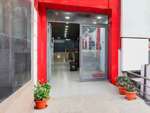 A modern building entrance with a red facade, glass doors, and potted plants.