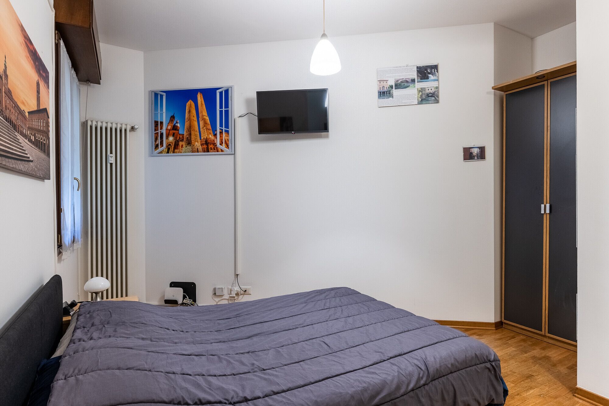 A bedroom with a bed, a TV, a radiator, a door, and a poster on the wall.