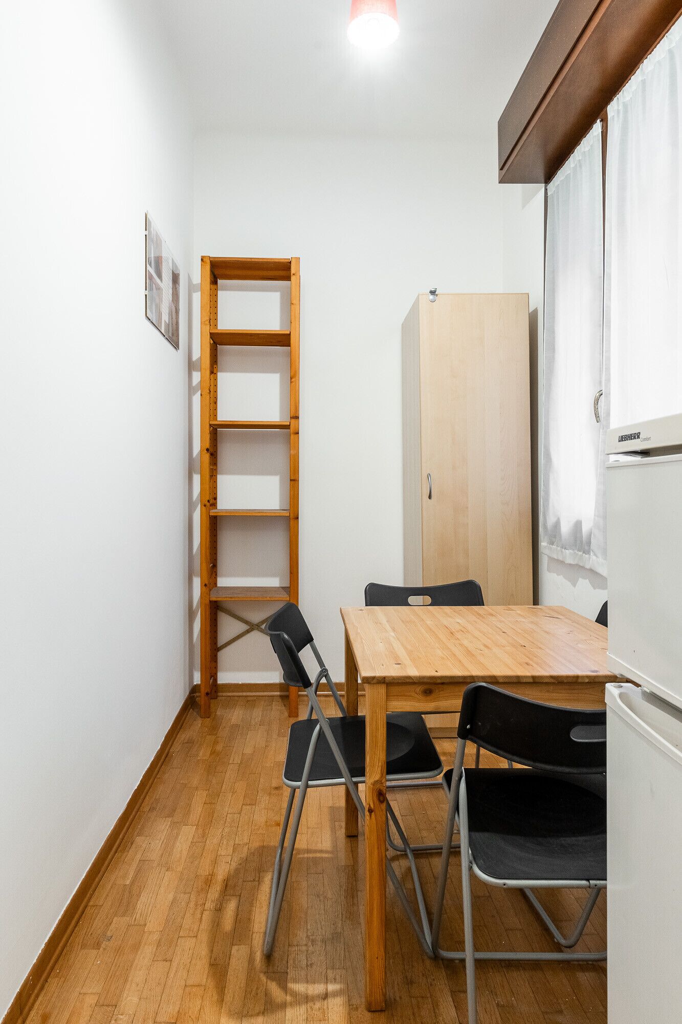Une petite pièce bien éclairée, avec une table en bois, quatre chaises, une échelle en bois, un meuble et une fenêtre avec des rideaux.