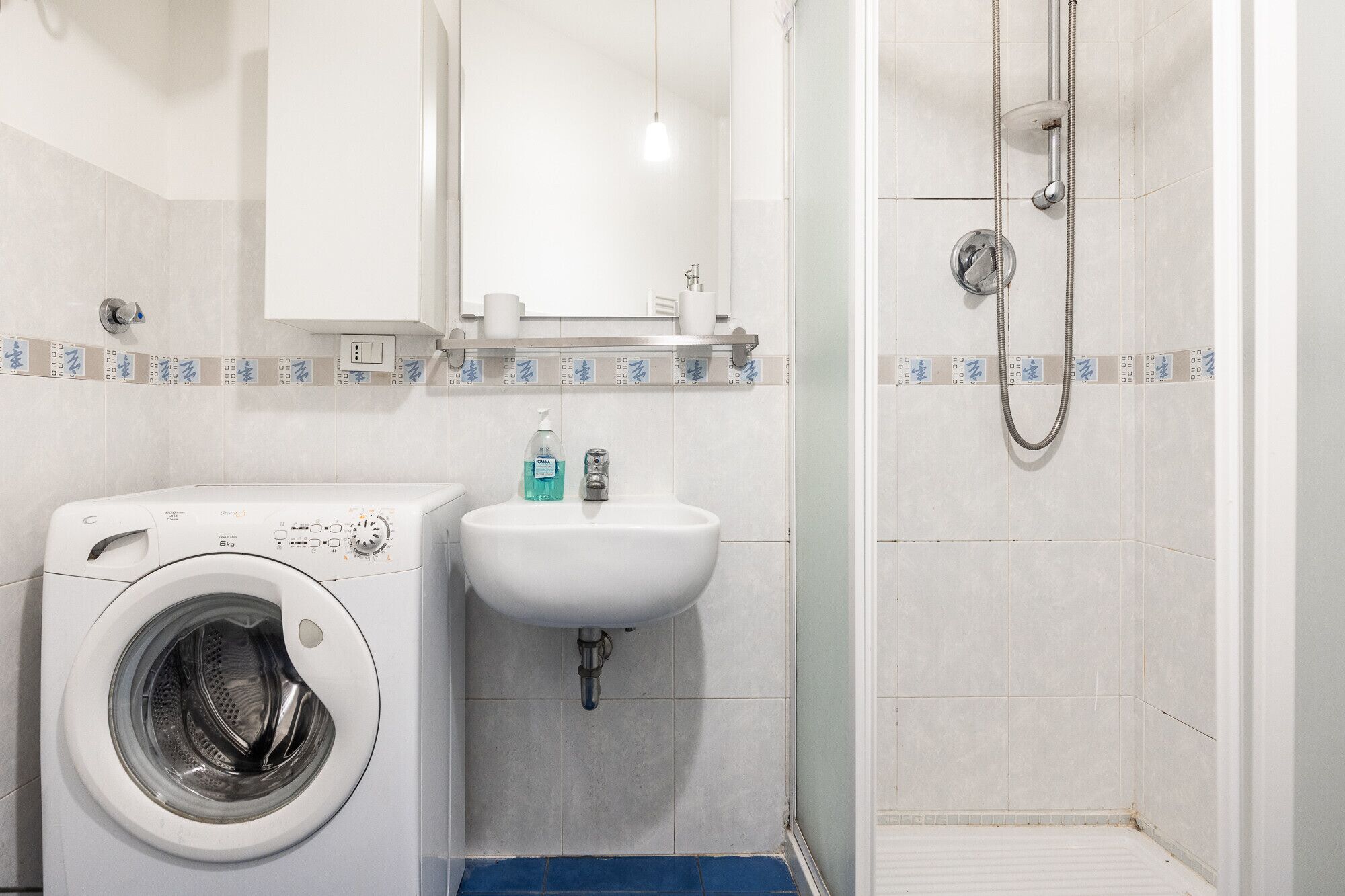 A compact bathroom with a washing machine, sink, and shower.