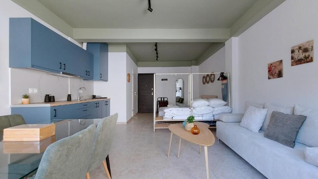 A modern living room with a sofa, a dining table with chairs, and a kitchen area with cabinets and a countertop.