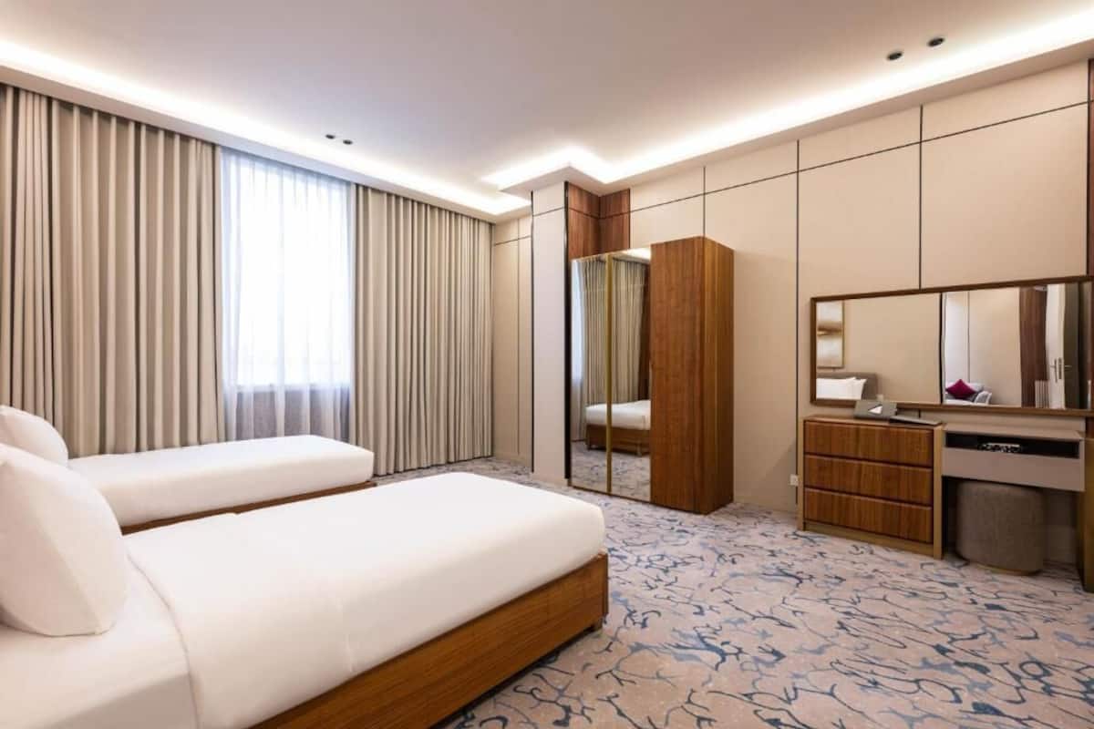 A hotel room with a bed, a desk, a mirror, a wardrobe, and a large window with curtains.