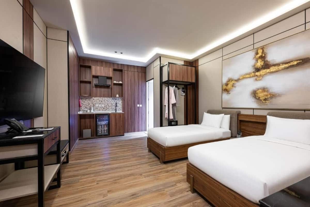 A modern hotel room with a wooden floor, a large bed, a TV, a wardrobe, and a painting on the wall.