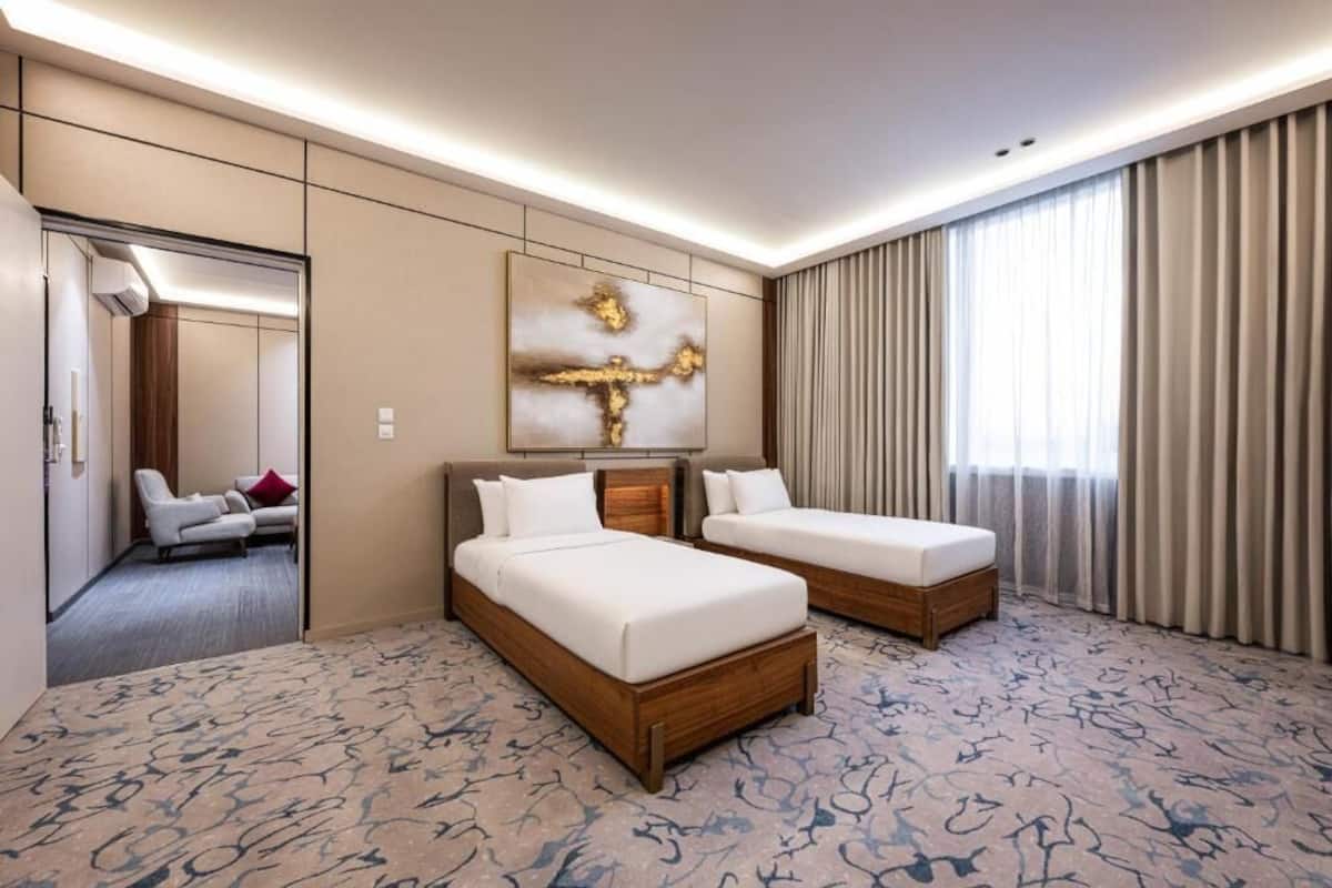 A hotel room with two beds, a large mirror, a wall art piece, and a view of another room.