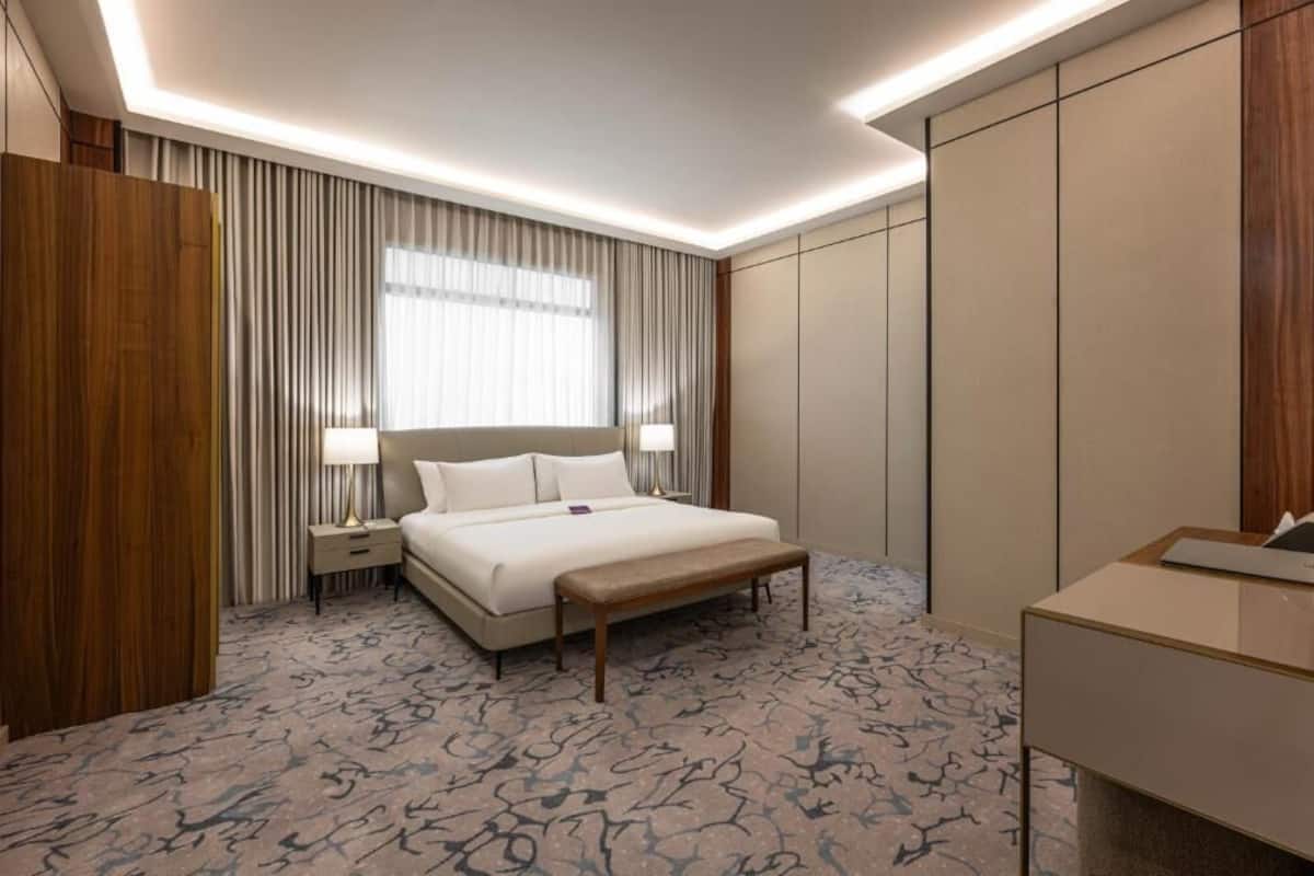 A hotel room with a bed, bedside tables, a bench, a desk, and a wardrobe.