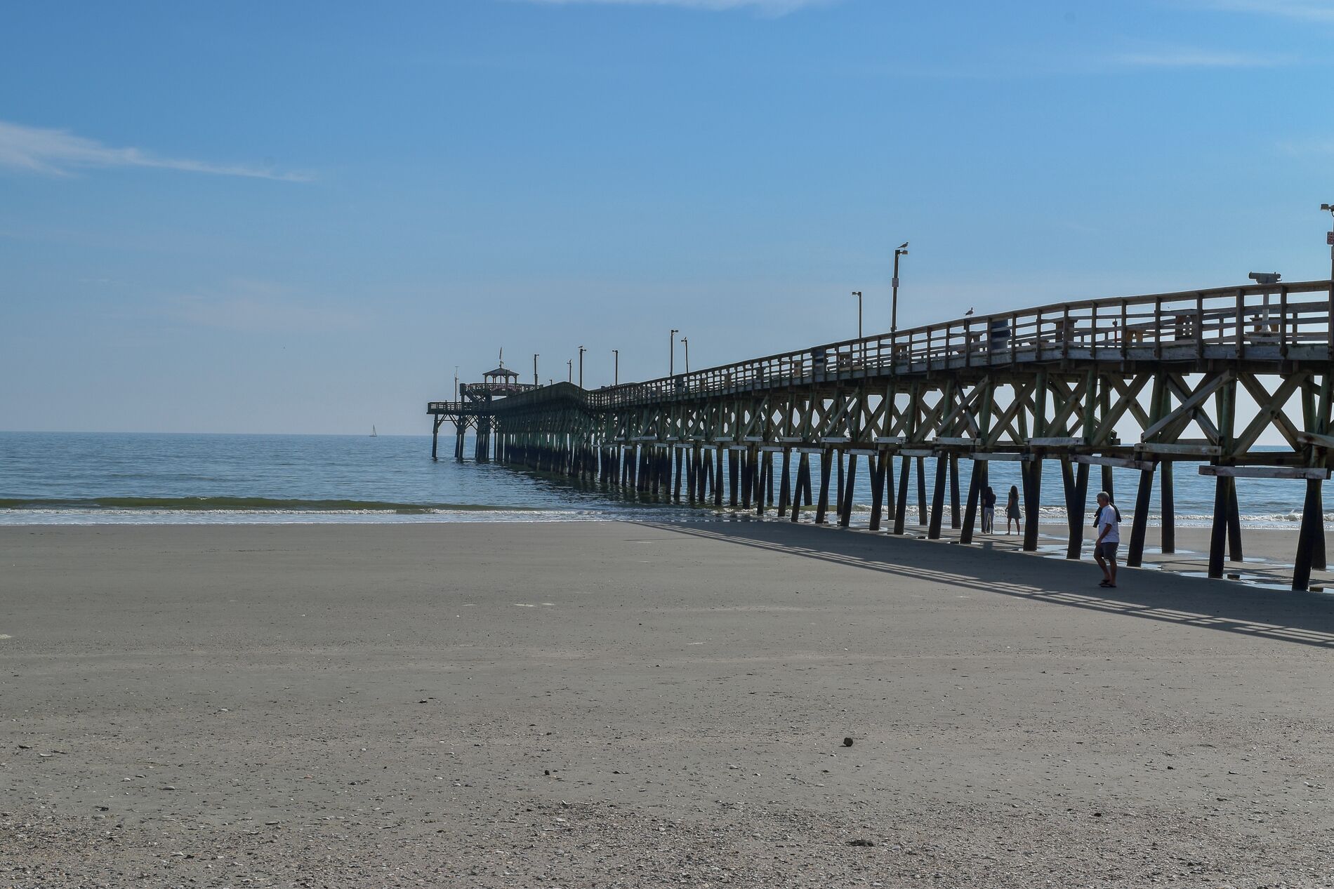 A pier extending into the water with a sandy beach in the foreground.