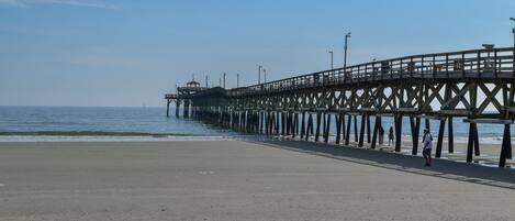 A pier extending into the water with a sandy beach in the foreground.