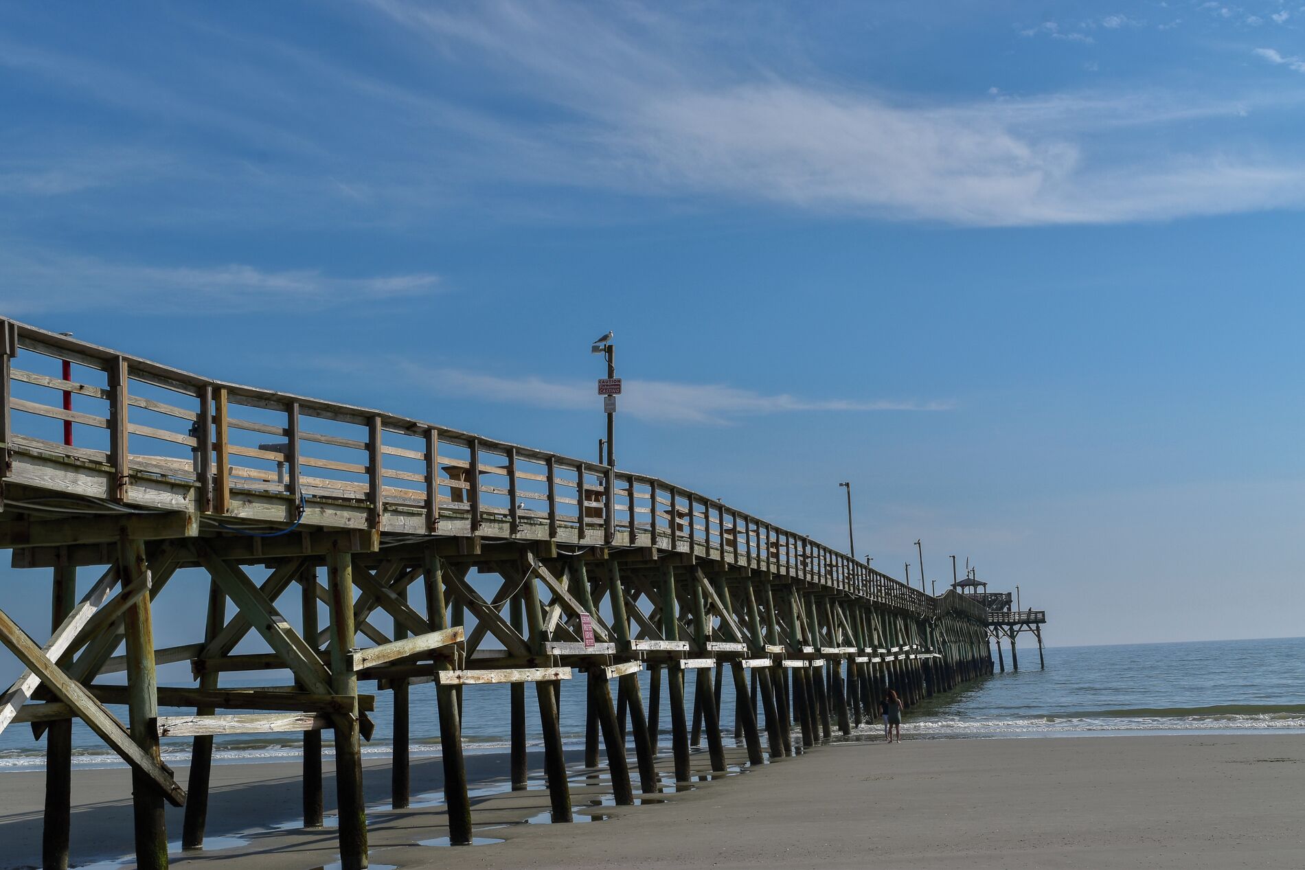 A wooden pier extending into the ocean with a railing and a caution sign.