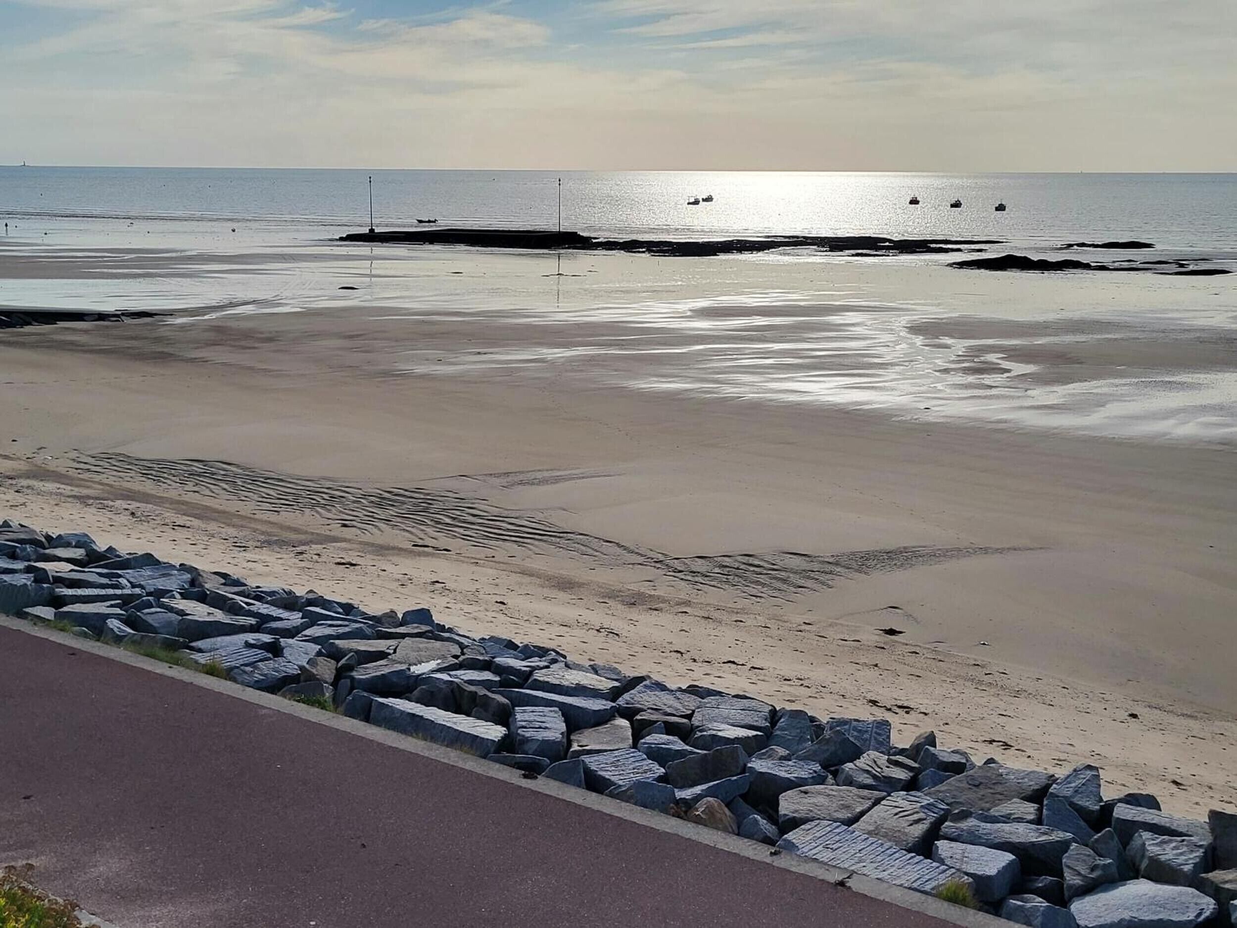 A beach with a rocky breakwater, calm sea, and clear skies.