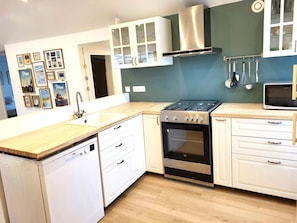 A kitchen with a dishwasher, stove, oven, and microwave. There are cabinets and a countertop. - Gîte Les Pirouettes: private terrace, garden & Wi-Fi steps from the beach (Pirou)