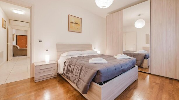 Un dormitorio con cama, mesitas de noche, un espejo y un cuadro en la pared.
