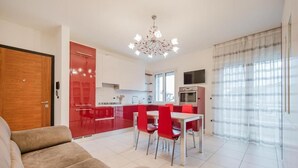 Una cocina moderna con armarios rojos, un comedor con sillas rojas, un sofá beige y una araña.