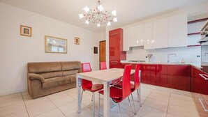 Una cocina moderna con armarios rojos, una mesa de comedor con sillas rojas, un sofá beige y una araña.