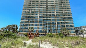 Ett högt hotell med flera balkonger, en sandstrand framför och palmer.