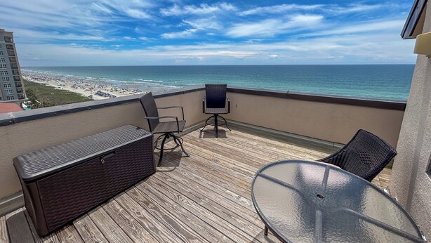 Ein Balkon mit Blick auf das Meer, Korbmöbel und ein Glastisch.