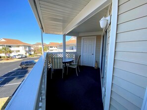 A covered balcony with a table and chairs, a door, and a view of a street with parked cars and buildings. - 2BR 2BA condo 2 blocks from beach. Easy beach access. Pool. (North Myrtle Beach)