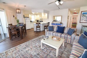 A living room with a sofa, a coffee table, and a dining area with chairs and a table. - 15% off 3-7 nights thru Sept 7. 2BR. 2 block easy walk to beach. Outdoor pool. (North Myrtle Beach)