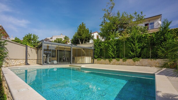 Une piscine dotée d’une enceinte en verre, entourée de verdure et d’un mur en pierre.
