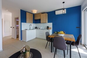 A modern kitchen with white cabinets, a wooden dining table, and a blue accent wall. - Modern apartment with swimming pool, private parking, sea view (Crikvenica)