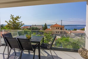 A balcony with a table and chairs, overlooking a residential area and a body of water. - Modern apartment with swimming pool, private parking, sea view (Crikvenica)