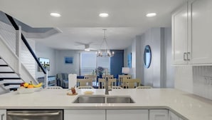 A modern kitchen with white cabinetry, a stainless steel sink, and a dining area with a chandelier. - Oceanfront Penthouse with Sweeping Atlantic Views | Wild Dunes | Isle of Palms (Isle of Palms)