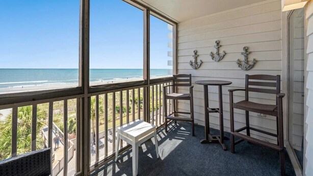 Un balcone con vista sulla spiaggia, sedie di legno, un tavolino e ancora decorative al muro.