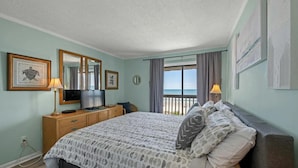 Una camera da letto con un letto, una cassettiera, una televisione e vista sulla spiaggia.