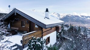Eine Holzhütte mit Balkon, Schornstein und Blick auf schneebedeckte Berge.