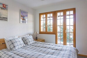 Une chambre à coucher avec un lit, une table de chevet, une lampe et une fenêtre donnant sur des arbres.