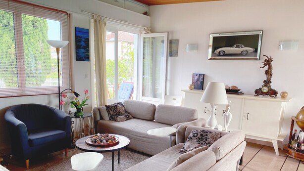 A living room with a sofa, armchair, coffee table, and a cabinet with a clock and decorative items. - Seaside Holiday Home: Spacious, Welcoming, Garden, Wi-Fi (Pornic)